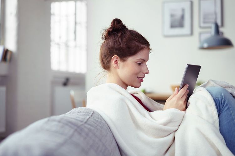 Junge Frau, die mit einem Tablet auf dem Sofa sitzt und sich zur Behandlung von Hyperhidrose informiert